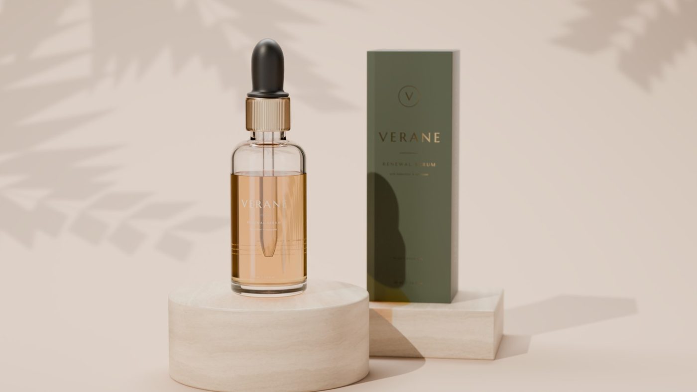 Amber dropper bottle and green gold-foil carton of a fictional skincare serum on travertine plinths, soft sunlight with palm-leaf shadows